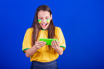 young girl, soccer fan from Brazil. holding cellphone, surprised. Smartphone. applications.