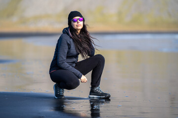 portrait woman walking on the black volcanic sand beach with mountains in the background. She is...