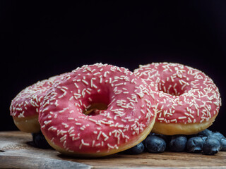 Plate with delicious pink donuts and healthy blueberries
