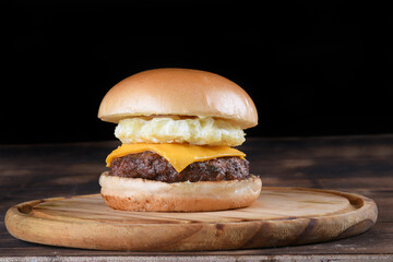 beef burger sandwich with cheese and fried egg soft bread, side view on wooden table isolated on black background