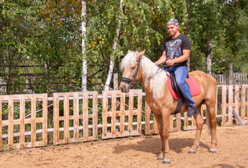 Outside on a beautiful warm day, a young man is riding a horse.