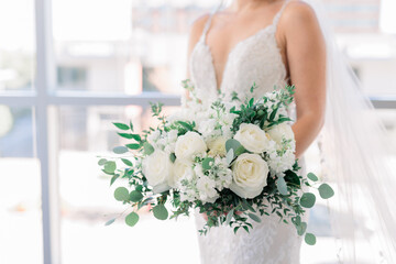 Bride is holding a white flower bouquet against her white wedding dress