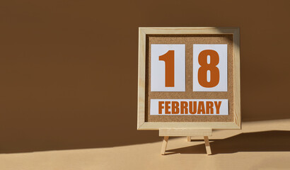 February 18th. Day 18 of month, Calendar date. Cork board, easel in sunlight on desktop. Close-up,...