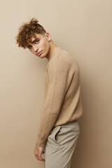 a handsome, attractive man in stylish clothes stands on a beige background sideways to the camera and poses relaxed