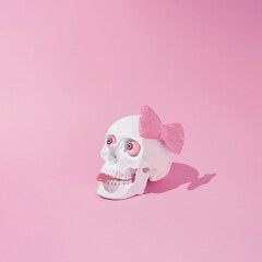 Skull with pink bow tie and tongue and eyes sticking out . Minimal spooky girl concept. Halloween pink background.