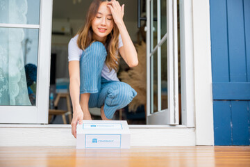 Close up hands of sick Asian woman sitting at door to receive medication first aid pharmacy box from hospital delivery service at floor home, merchandise medicine online business, healthcare concept - obrazy, fototapety, plakaty