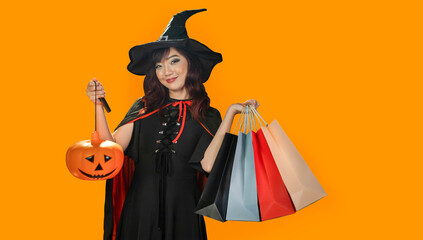 Asian girl in witch costume holding jack o lantern and shopping sale bag for halloween party trick or treat concept isolate on orange background