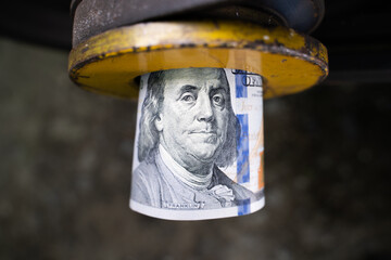 Benjamin Franklin on a 100 dollar bill rolled into a tube. Money in an industrial mechanism. Yellow...