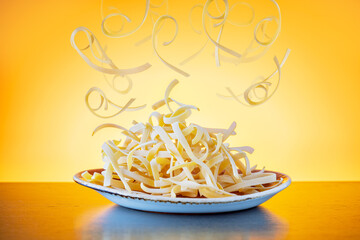 Uncooked dried pasta in plate and flying yellow raw pasta over yellow background.