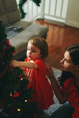 Caucasian girl and mom in red clothes decorating fir tree on Christmas holidays