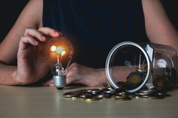 Woman holds lightbulb with jar and coin. Saving money, investment, banking and finance concept.