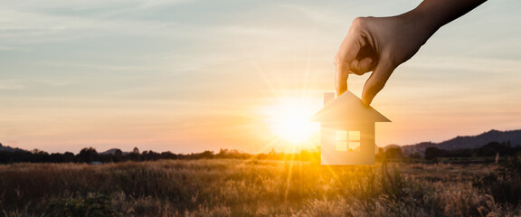Woman's hands holding paper house at sunset evening.family home,real estate,homeless...