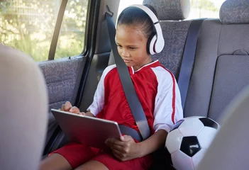 Rolgordijnen Tablet, sports and relax child on car travel transportation to soccer, football or match game in SUV van with safety seat belt. Youth girl streaming video, subscription movie or use kid friendly app © Nina Lawrenson/peopleimages.com