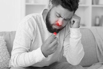 Young bearded man with nosebleed and tissue at home