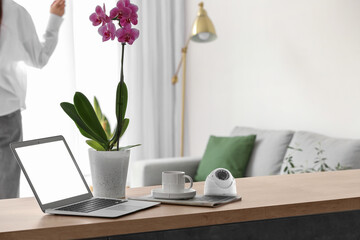 Modern security CCTV camera with laptop, cup of coffee and orchid plant on table in room