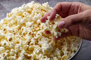 Female hand holds popcorn on grey concrete background.