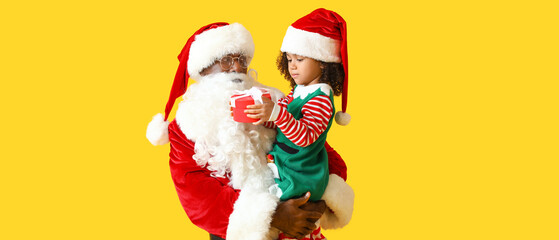 Little African-American girl with gift and Santa Claus on yellow background