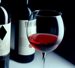 glass of red wine slightly over angled and flanked by wine bottles - dark background