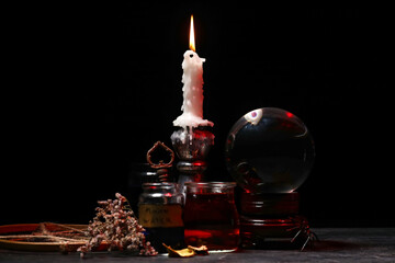 Burning candle, jars with potion and crystal ball on dark background