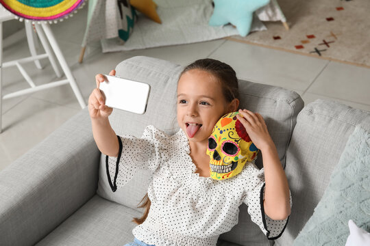 Little Mexican girl with painted human skull taking selfie at home