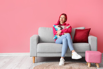 Obraz premium Pretty young woman with unusual hair sitting on sofa against pink background