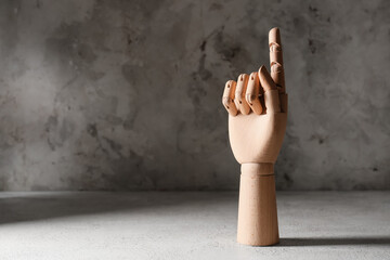 Wooden hand with raised index finger on grey grunge background