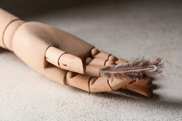 Wooden hand with pheasant feather grey background