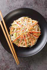 Japanese kani salad with crab sticks, glass vermicelli, carrot, cucumber and sesame seeds dressed with mayonnaise close-up in a plate on the table. vertical top view from above