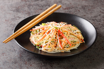 Kani salad made of crab meat and julienne vegetables, all doused in a sweet, spicy, and creamy dressing closeup in the plate on the table. Horizontal