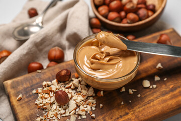 Wooden board with bowl of tasty hazelnut butter on table, closeup