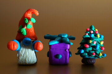 A gnome figurine with a gift and a Christmas tree on a brown background. Christmas toys and decorations.