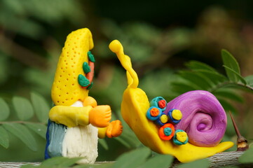 A figure of a joyful gnome and a snail. Objects made of plasticine. Fairy-tale characters.