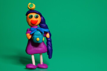 A plasticine toy girl with a gift on a green background.
