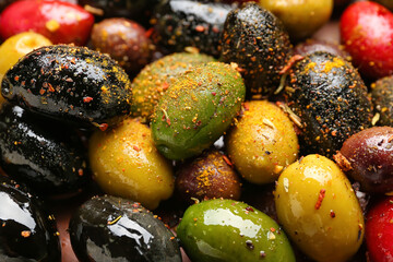 Different kinds of delicious olives with spices as background, closeup