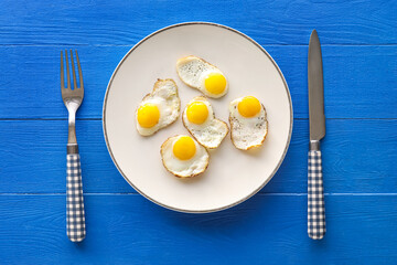 Plate with tasty fried quail eggs on blue wooden background