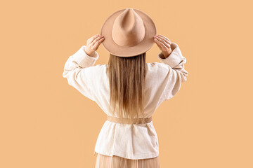 Beautiful fashionable young woman in hat and knitted sweater on beige background, back view