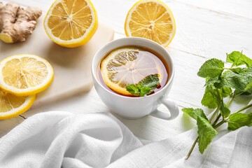 Cup of black tea with lemon and mint on white table, closeup