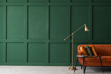 Table with magazine, red sofa and lamp near green wall