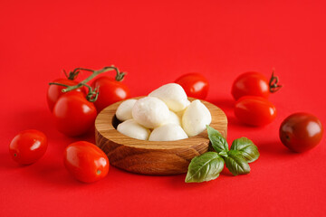 Wooden bowl with delicious mozzarella cheese and tomatoes on color background