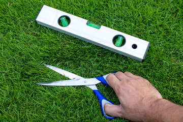 Cutting the grass with scissors and using level tool to level the lawn