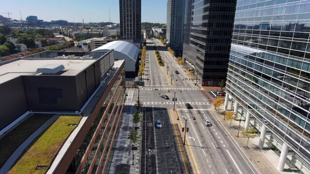 aerial footage along a street with cars and trucks driving surrounded by skyscrapers and office buildings in the city skyline and lush green trees with a gorgeous clear blue sky in Atlanta Georgia USA