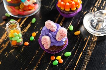 Tasty Halloween cupcakes with candies on dark wooden background, closeup