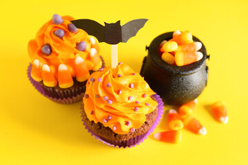 Tasty Halloween cupcakes and cauldron with candy corns on yellow background