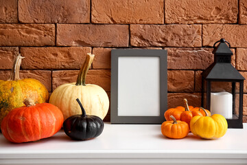 Blank frame with Halloween pumpkins and lantern on mantelpiece near brick wall