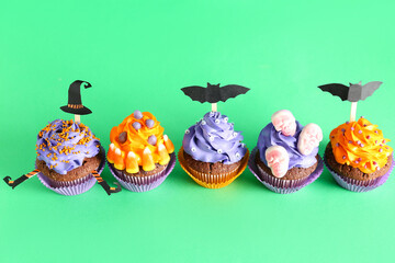 Tasty Halloween cupcakes on green background