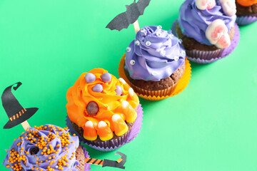 Tasty Halloween cupcakes on green background