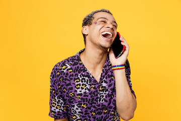 Young smiling happy fun gay man wear purple animal print shirt doing selfie shot on mobile cell phone isolated on bright plain yellow color background studio portrait. Lifestyle lgbtq pride concept