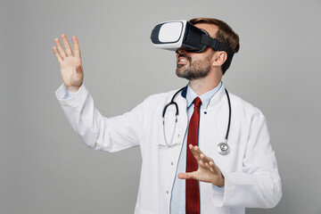 Male doctor intern man wears white medical gown suit work in hospital watching in vr headset pc gadget play game isolated on plain grey color background studio portrait. Healthcare medicine concept.