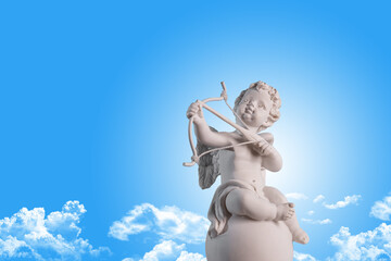 Figurine of an angel Cupid on the podium with a bow and arrow on a blu sky with clouds background ....