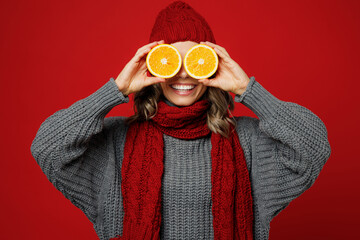 Young happy woman wear grey sweater scarf hat hold cover eyes with half of oranges isolated on...